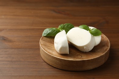 Photo of Pieces of delicious mozzarella cheese and basil leaves on wooden table, closeup. Space for text