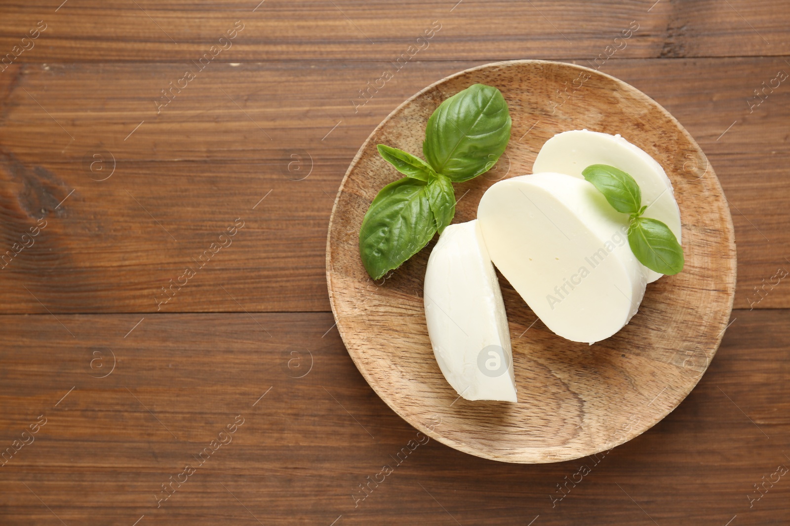 Pieces of delicious mozzarella cheese and basil leaves on wooden table, top view. Space for text Photo of Pieces of delicious mozzarella cheese and basil leaves on wooden table, top view. Space for text