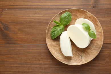 Photo of Pieces of delicious mozzarella cheese and basil leaves on wooden table, top view. Space for text