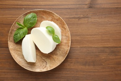 Photo of Pieces of delicious mozzarella cheese and basil leaves on wooden table, top view. Space for text