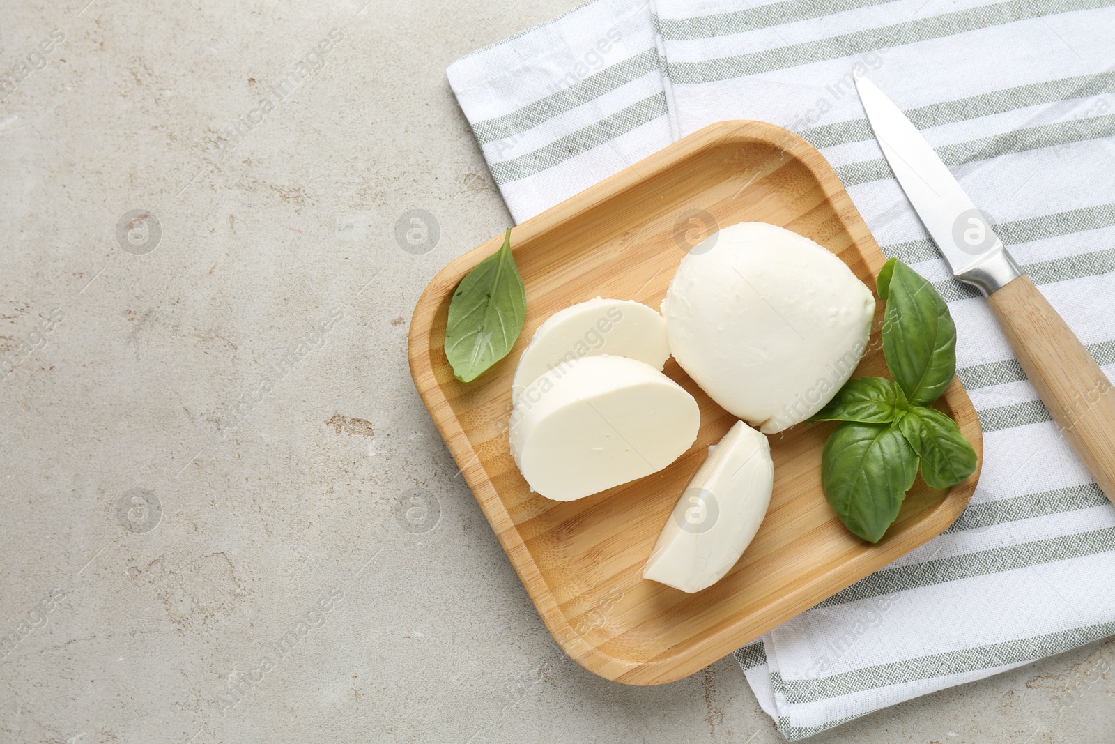 Pieces of delicious mozzarella cheese, basil leaves and knife on grey textured table, flat lay. Space for text Photo of Pieces of delicious mozzarella cheese, basil leaves and knife on grey textured table, flat lay. Space for text