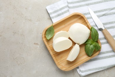 Photo of Pieces of delicious mozzarella cheese, basil leaves and knife on grey textured table, flat lay. Space for text