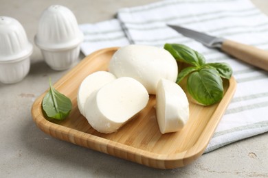 Photo of Pieces of delicious mozzarella cheese and basil leaves on grey textured table, closeup