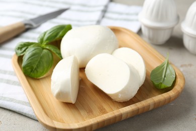 Photo of Pieces of delicious mozzarella cheese and basil leaves on grey textured table, closeup