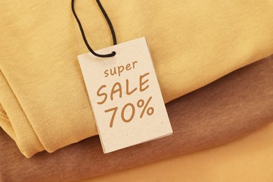 Image of Sale tag and clothes on pale brown background, closeup