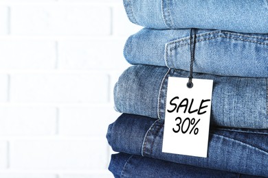 Image of Sale tag and stack of jeans against white brick wall, closeup