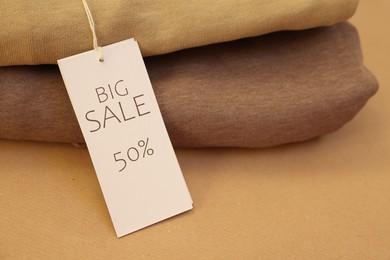 Image of Sale tag and clothes on pale brown background, closeup