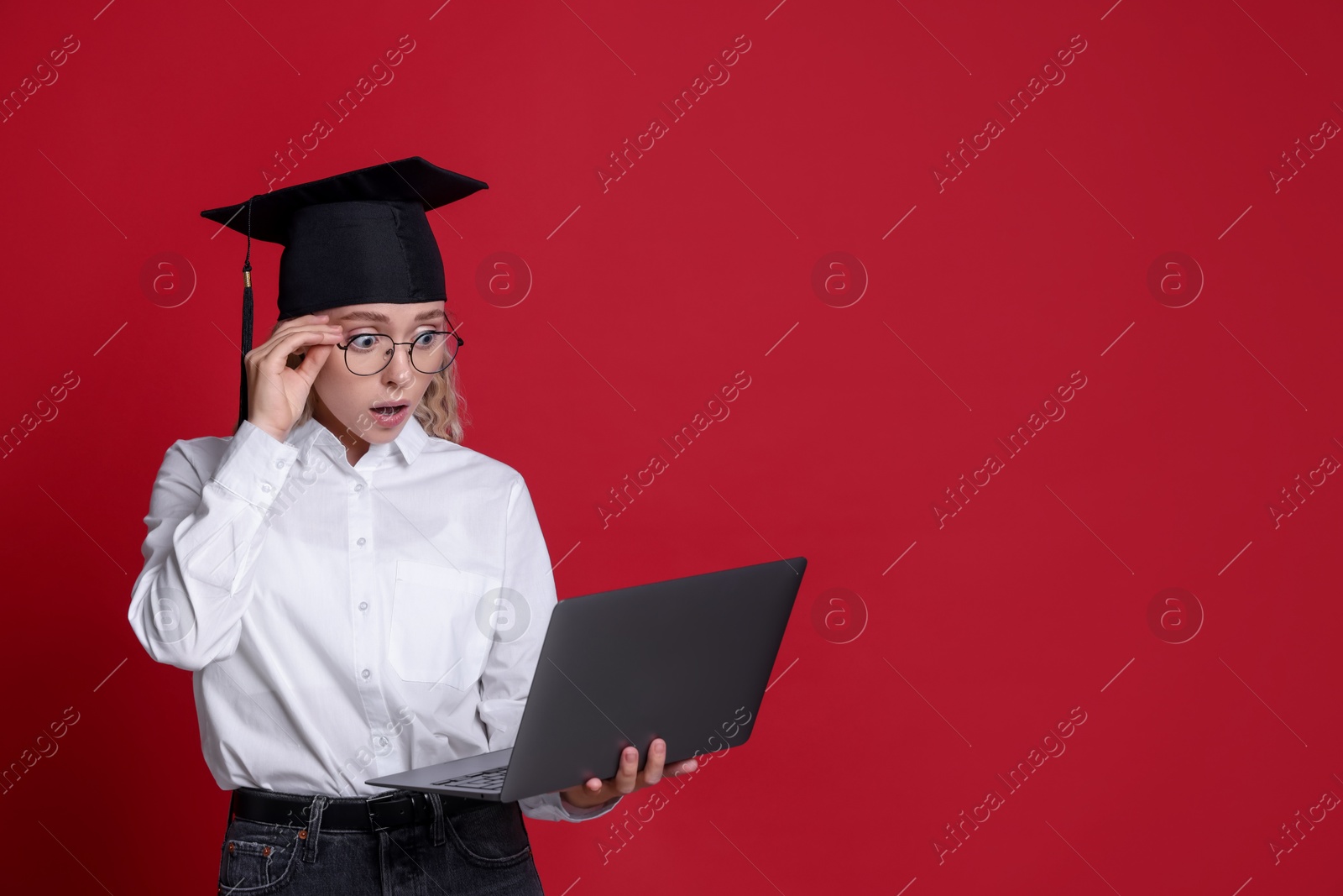 Excited student with laptop before graduation on red background. Space for text Photo of Excited student with laptop before graduation on red background. Space for text