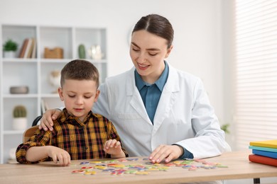 Photo of Dyslexia treatment. Pediatrician working with little boy at table indoors