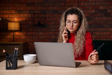Photo of Woman talking by smartphone at desk with laptop in home office