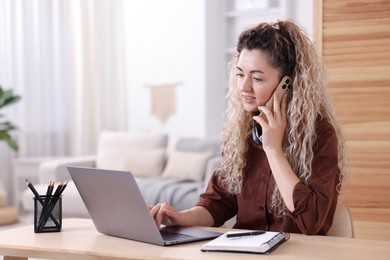 Photo of Smiling woman talking by smartphone at desk with laptop in home office