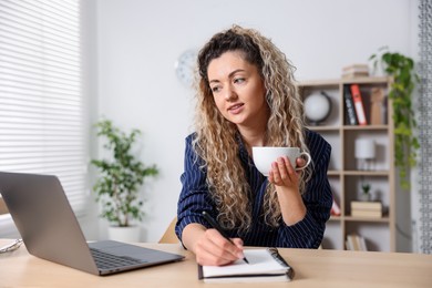 Photo of Woman with cup of hot drink working at desk in home office