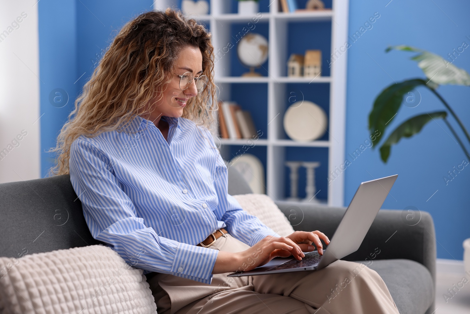 Smiling woman working with laptop on sofa in home office Photo of Smiling woman working with laptop on sofa in home office