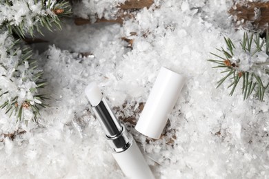 Photo of Moisturizing lip balm and fir tree branches on artificial snow, above view. Winter care
