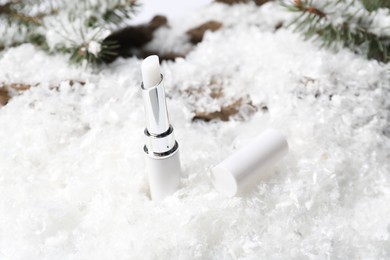 Photo of Moisturizing lip balm and fir tree branches on artificial snow, closeup. Winter care