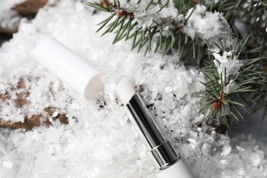 Photo of Moisturizing lip balm and fir tree branches on artificial snow, closeup. Winter care