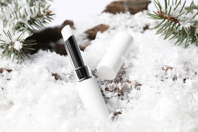 Photo of Moisturizing lip balm and fir tree branches on artificial snow, closeup. Winter care