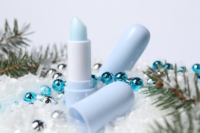 Photo of Moisturizing lip balms, Christmas decor and fir tree branches on artificial snow, closeup. Winter care