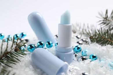 Photo of Moisturizing lip balms, Christmas decor and fir tree branches on artificial snow, closeup. Winter care