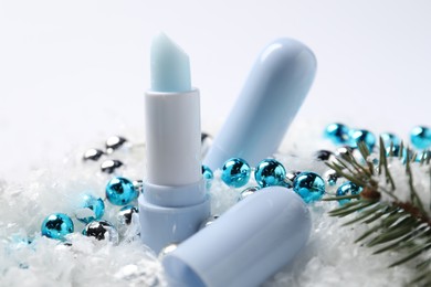 Photo of Moisturizing lip balms, Christmas decor and fir tree branches on artificial snow, closeup. Winter care