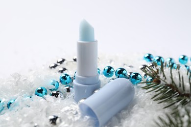 Photo of Moisturizing lip balm, Christmas decor and fir tree branches on artificial snow, closeup. Winter care