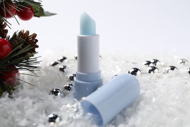 Photo of Moisturizing lip balm and Christmas decor on artificial snow, closeup. Winter care