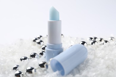 Photo of Moisturizing lip balm and Christmas decor on artificial snow, closeup. Winter care