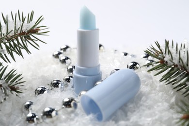 Photo of Moisturizing lip balm, Christmas decor and fir tree branches on artificial snow, closeup. Winter care