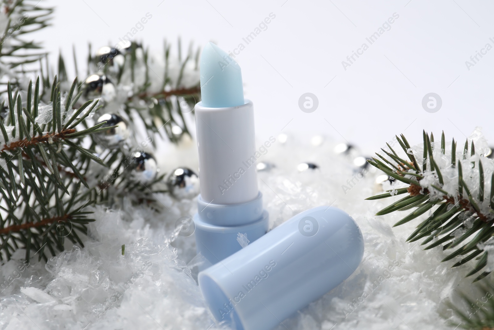 Moisturizing lip balm, Christmas decor and fir tree branches on artificial snow, closeup. Winter care Photo of Moisturizing lip balm, Christmas decor and fir tree branches on artificial snow, closeup. Winter care
