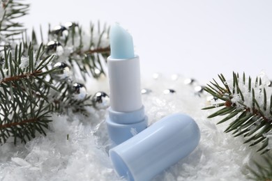 Photo of Moisturizing lip balm, Christmas decor and fir tree branches on artificial snow, closeup. Winter care