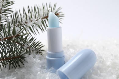 Photo of Moisturizing lip balm and fir tree branches on artificial snow, closeup. Winter care