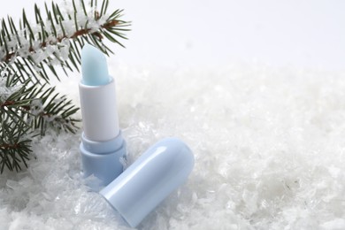 Photo of Moisturizing lip balm and fir tree branches on artificial snow, closeup. Space for text