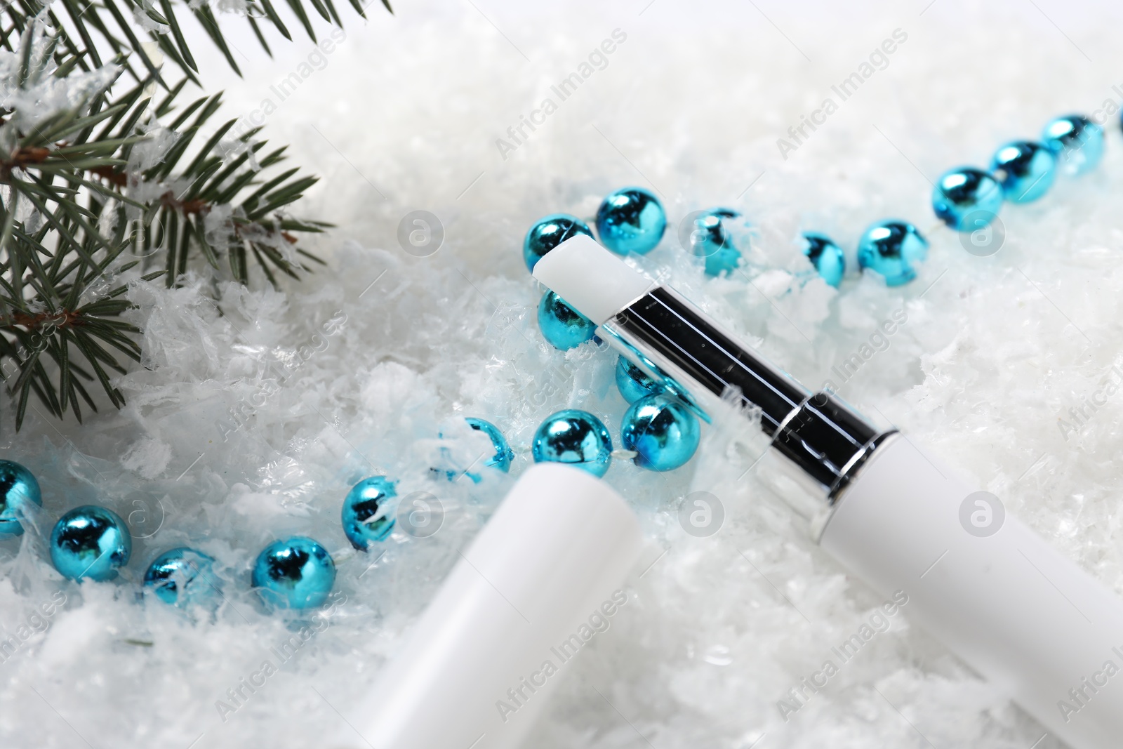 Photo of Moisturizing lip balm, Christmas decor and fir tree branches on artificial snow, closeup. Winter care
