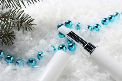 Photo of Moisturizing lip balm, Christmas decor and fir tree branches on artificial snow, closeup. Winter care