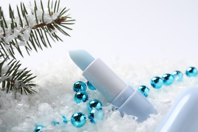 Photo of Moisturizing lip balm, Christmas decor and fir tree branches on artificial snow, closeup. Winter care