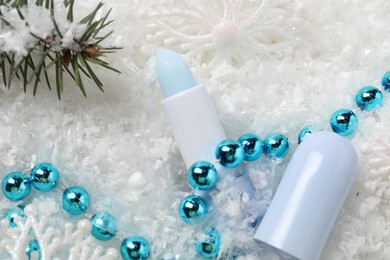 Photo of Moisturizing lip balm, Christmas decor and fir tree branches on artificial snow, flat lay. Winter care