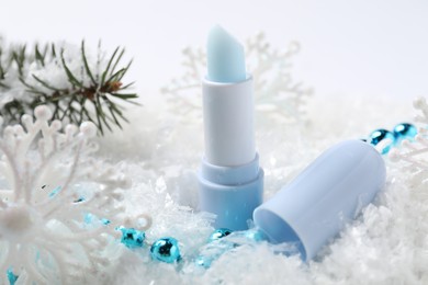 Photo of Moisturizing lip balm, Christmas decor and fir tree branches on artificial snow, closeup. Winter care