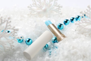 Photo of Moisturizing lip balm and Christmas decor on artificial snow, closeup. Winter care