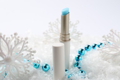 Photo of Moisturizing lip balm and Christmas decor on artificial snow, closeup. Winter care
