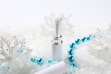 Photo of Moisturizing lip balm and Christmas decor on artificial snow, closeup. Winter care