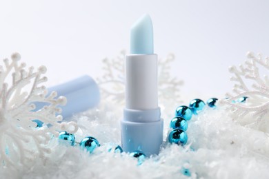Photo of Moisturizing lip balm and Christmas decor on artificial snow, closeup. Winter care