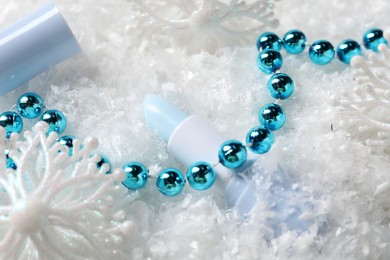 Photo of Moisturizing lip balm and Christmas decor on artificial snow, closeup. Winter care