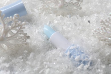 Photo of Moisturizing lip balm and Christmas decor on artificial snow, closeup. Winter care