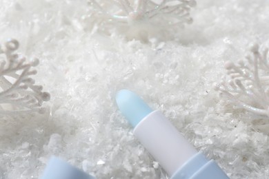 Photo of Moisturizing lip balm and Christmas decor on artificial snow, closeup. Winter care