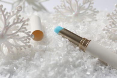 Photo of Moisturizing lip balm and Christmas decor on artificial snow, closeup. Winter care