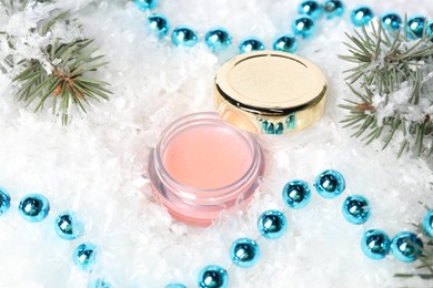 Photo of Moisturizing lip balm, Christmas decor and fir tree branches on artificial snow, closeup. Winter care