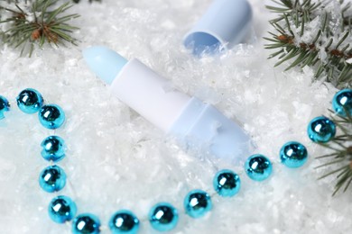 Photo of Moisturizing lip balm, Christmas decor and fir tree branches on artificial snow, closeup. Winter care