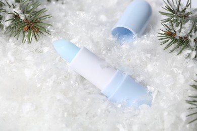 Photo of Moisturizing lip balm and fir tree branches on artificial snow, closeup. Winter care