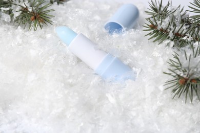 Photo of Moisturizing lip balm and fir tree branches on artificial snow, closeup. Winter care