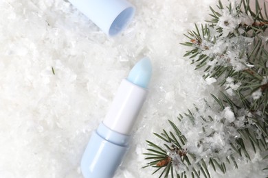 Photo of Moisturizing lip balm and fir tree branches on artificial snow, flat lay. Winter care